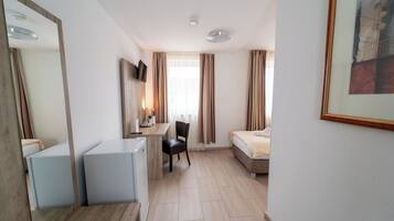 Habitación de hotel con cama, escritorio con silla, refrigerador pequeño y televisor montado en la pared.