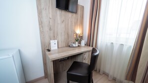 Ein kleiner, moderner Raum mit einem Holztisch, einem schwarzen Stuhl, einem flachbildfernseher an der Wand und einem Fenster mit durchsichtigen Vorhängen.