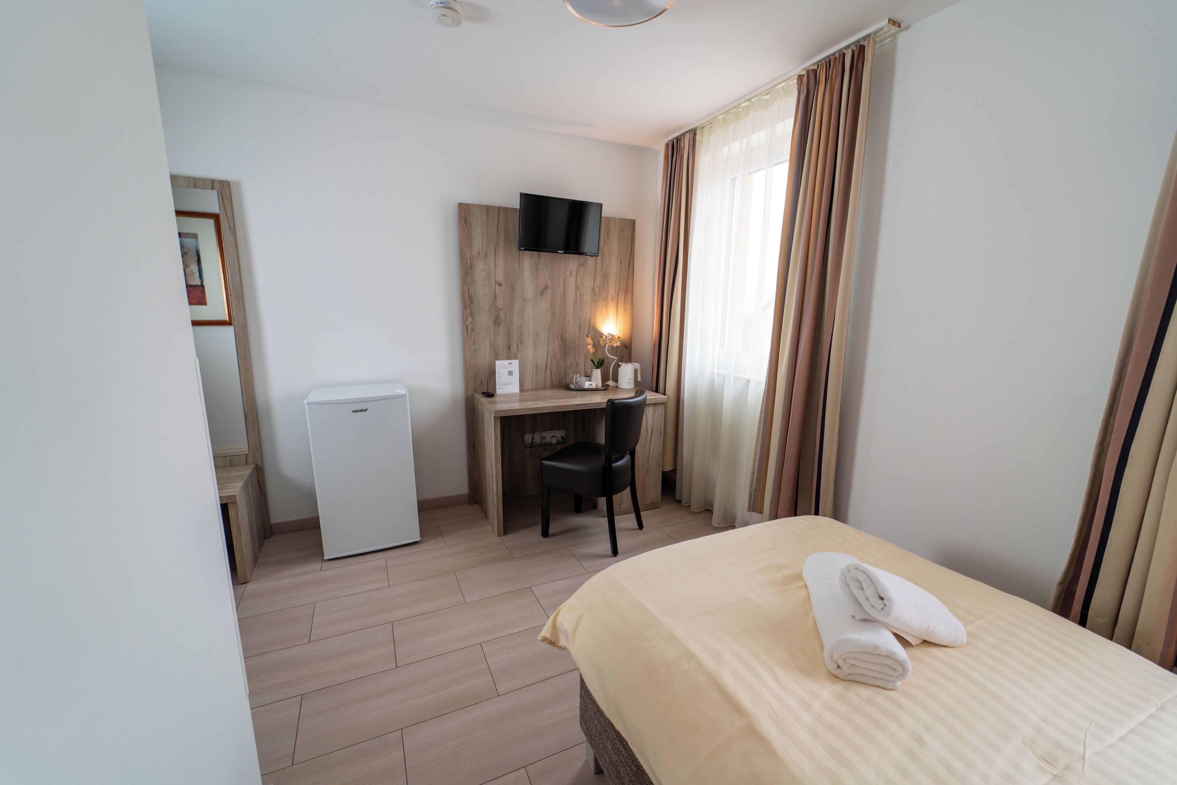 Habitación de hotel con cama, escritorio, silla, televisor y un refrigerador pequeño.