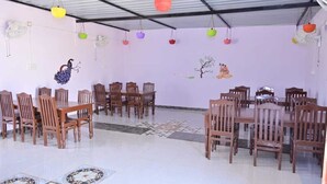 A spacious room with multiple wooden tables and chairs, a tiled floor, and colorful hanging lanterns. - Shourya Desert Camp (Jaisalmer)