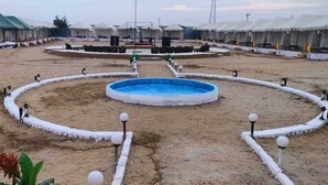 A circular pool with a blue center, surrounded by white pathways and lamp posts, with yurts in the background. - Shourya Desert Camp (Jaisalmer)