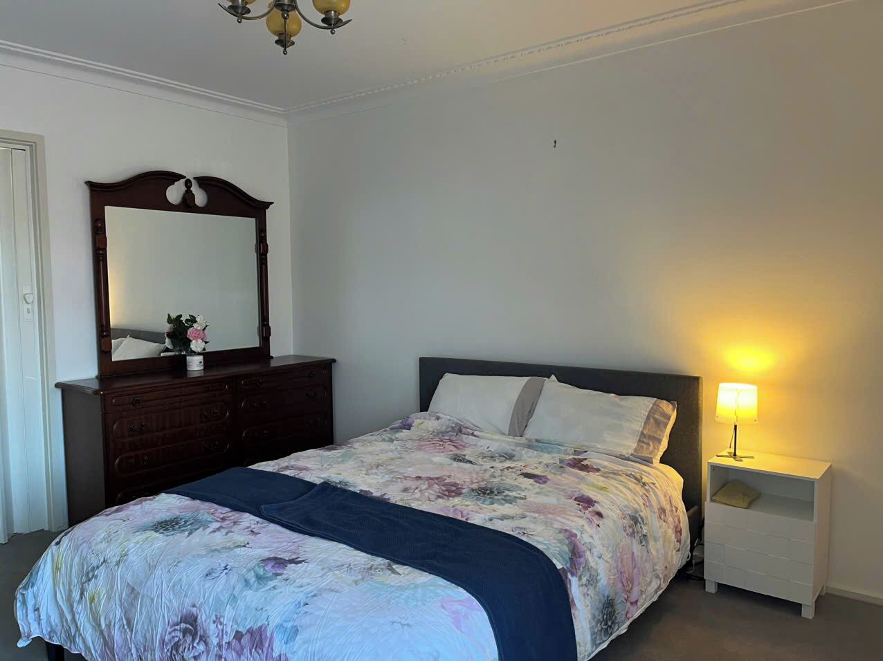 A bedroom with a bed, a dresser, a nightstand, and a mirror.