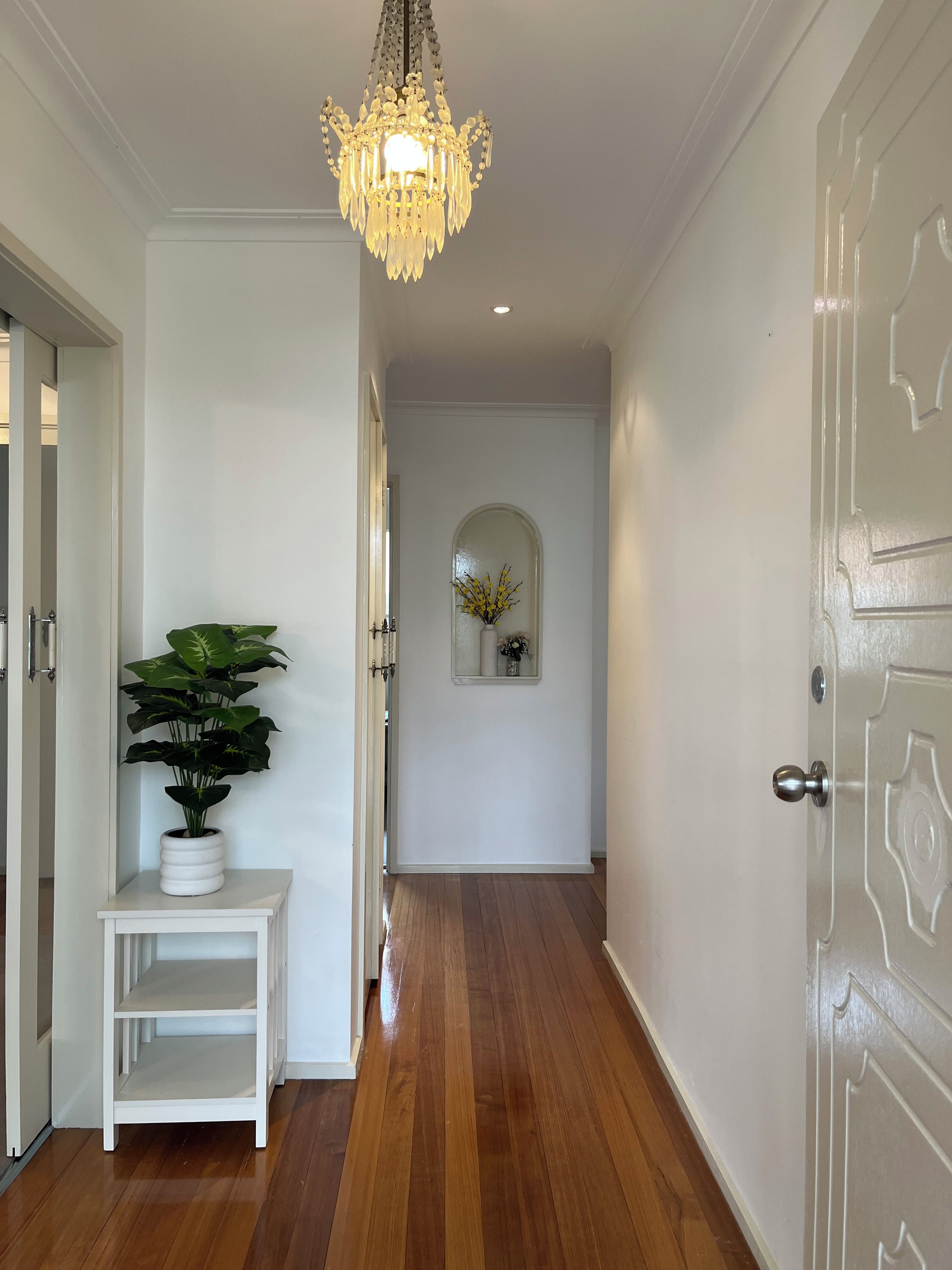 A hallway with a white door, a potted plant, a small table, and a decorative mirror.
