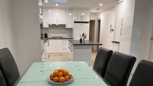Eine moderne Küche mit weißen Schränken, einem Glastisch und einer Schüssel mit Orangen sowie schwarzen Stühlen.