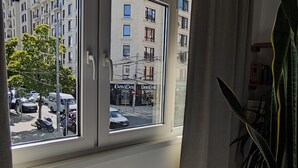 Una habitación con un ventanal grande que da a una calle y edificios. Hay una planta en maceta sobre una mesa.