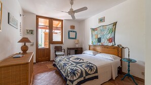 A bedroom with a bed, a desk, a chair, a ceiling fan, and a window.