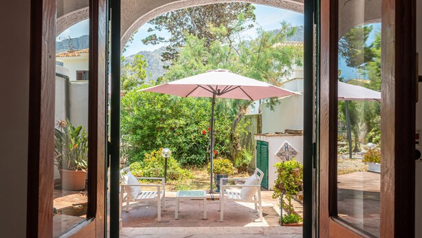 An open door leading to a patio with a table and chairs, an umbrella, and potted plants.