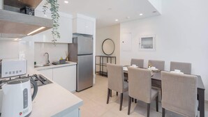 A modern kitchen with a refrigerator, stove, and kettle. There is a dining area with a table and chairs.