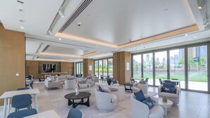 A spacious lounge area with multiple seating options, large windows offering views of the city, and a modern ceiling design.