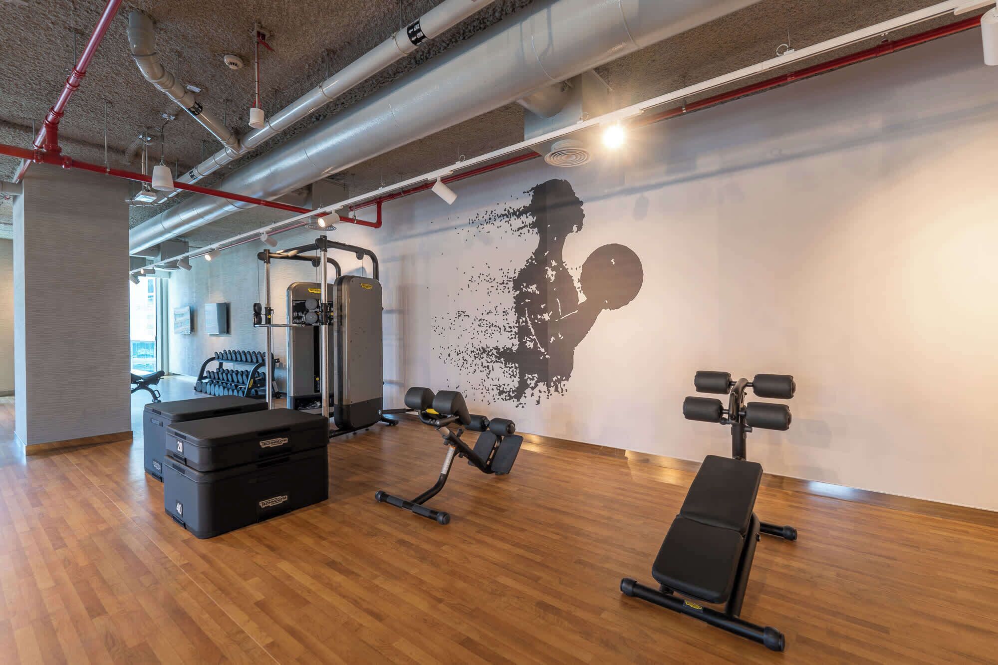 A gym with exercise equipment, a wall mural, and wooden flooring.
