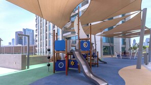 A playground with a slide and climbing structures, surrounded by a cityscape view.