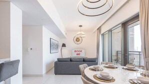 Un espace repas moderne avec une table ronde pour quatre personnes, un canapé gris et un panneau indiquant « RÉSERVEZ-MOI » accroché au mur.