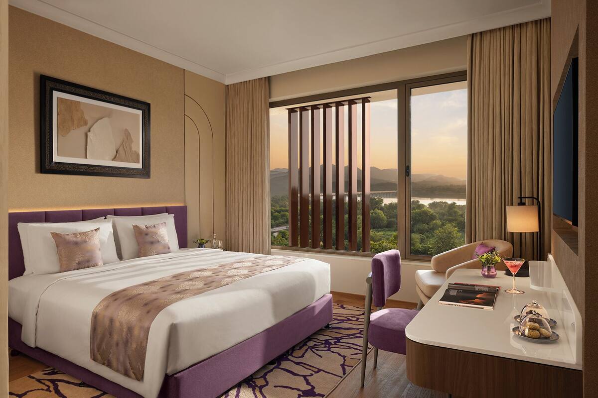 A hotel room with a bed, a desk, a chair, a TV, and a window with a view.