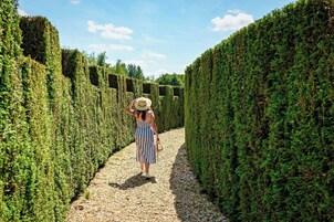 A woman walking down a gravel path flanked by neatly trimmed hedges.