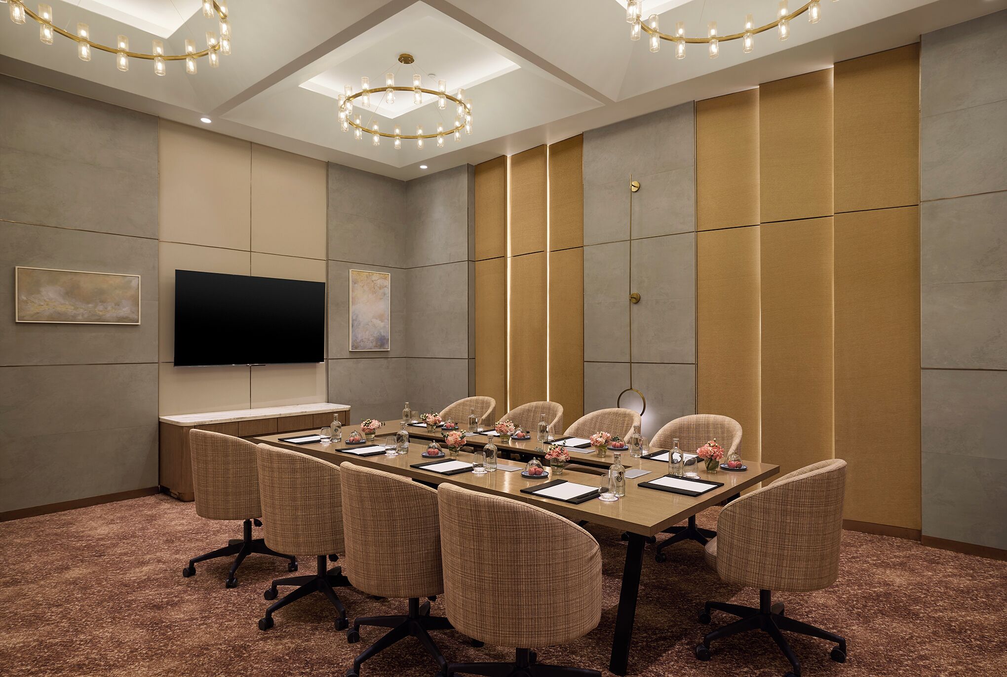 A conference room with a long table, chairs, a flat-screen TV, and a ceiling light fixture.