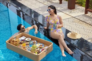 A poolside setting with a wicker tray containing food and drinks, a hat, and a person in a swimsuit.