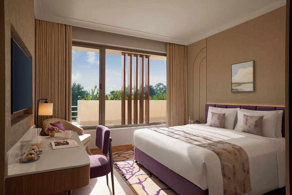 A hotel room with a bed, a desk with a chair, a TV, and a window with curtains.