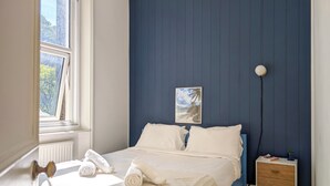 Un dormitorio con cama, mesita de noche, lámpara y ventana.