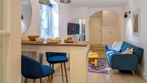 Una sala de estar moderna con un sofá azul, una mesita de centro y una zona de cocina con una mesa de comedor y taburetes de bar.