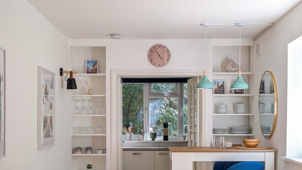 Una cocina compacta con ventana, muebles blancos y una silla azul.