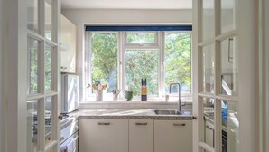 Una cocina con armarios blancos, encimera de granito, ventana con vistas a la vegetación y un lavamanos.