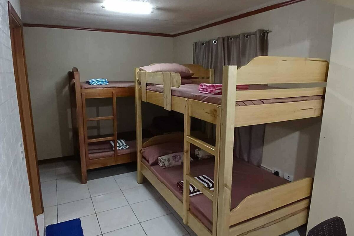 A bunk bed room with a desk and chair, a small shelf, and a window with curtains.