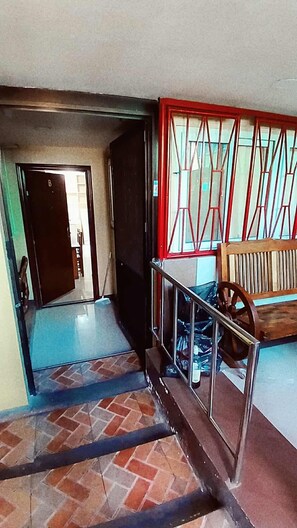 Un escalier avec une rampe en métal menant à une pièce dotée d’une fenêtre à cadre rouge et d’un banc en bois.