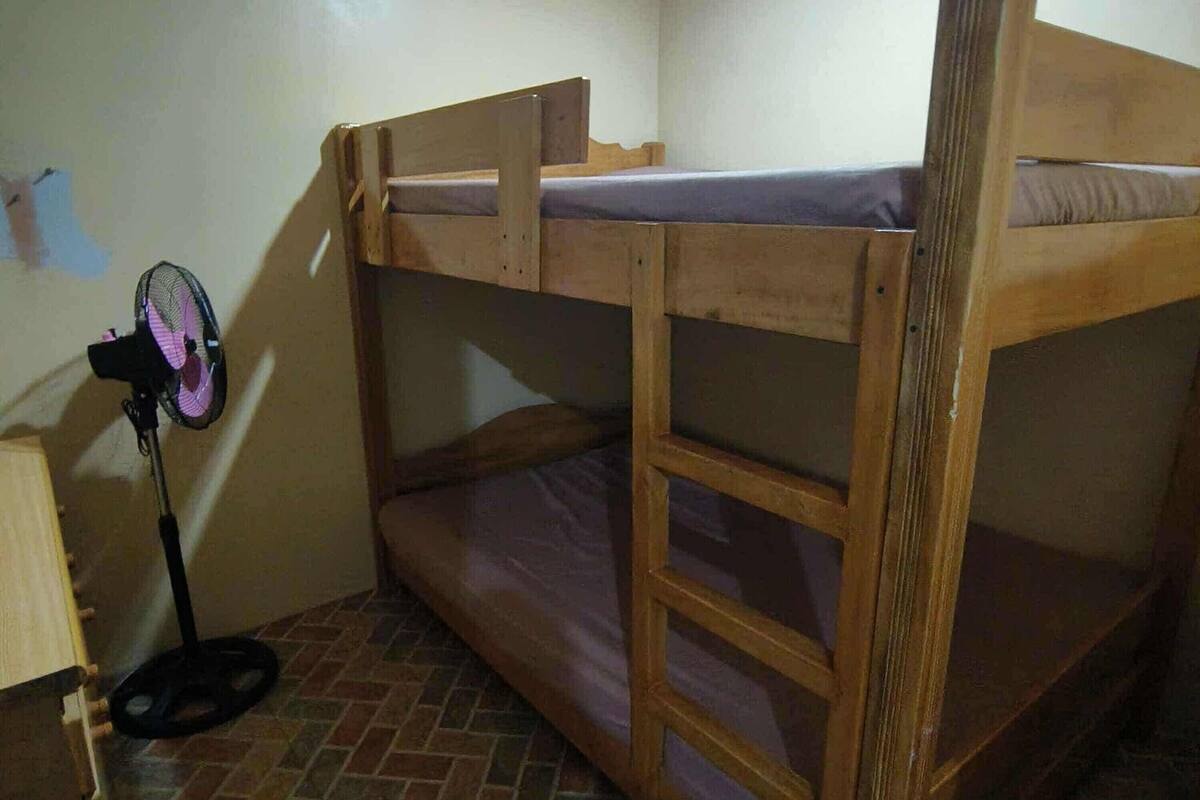 A bunk bed with a ladder, a standing fan, and a tiled floor.