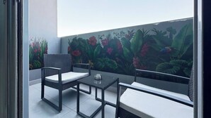Un balcon doté d’un espace salon, d’une table et d’une fresque représentant des plantes tropicales.