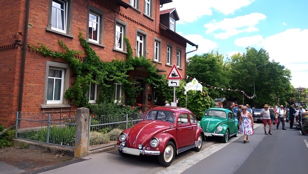 Un coche antiguo rojo y verde estacionado en una calle con un edificio de ladrillo y una señal de tráfico triangular.