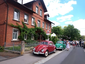 A red and green vintage car parked on a street with a brick building and a triangular road sign.