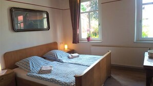 Une chambre avec un lit en bois, une lampe de chevet, une fenêtre donnant sur un paysage verdoyant et un tableau encadré au mur.