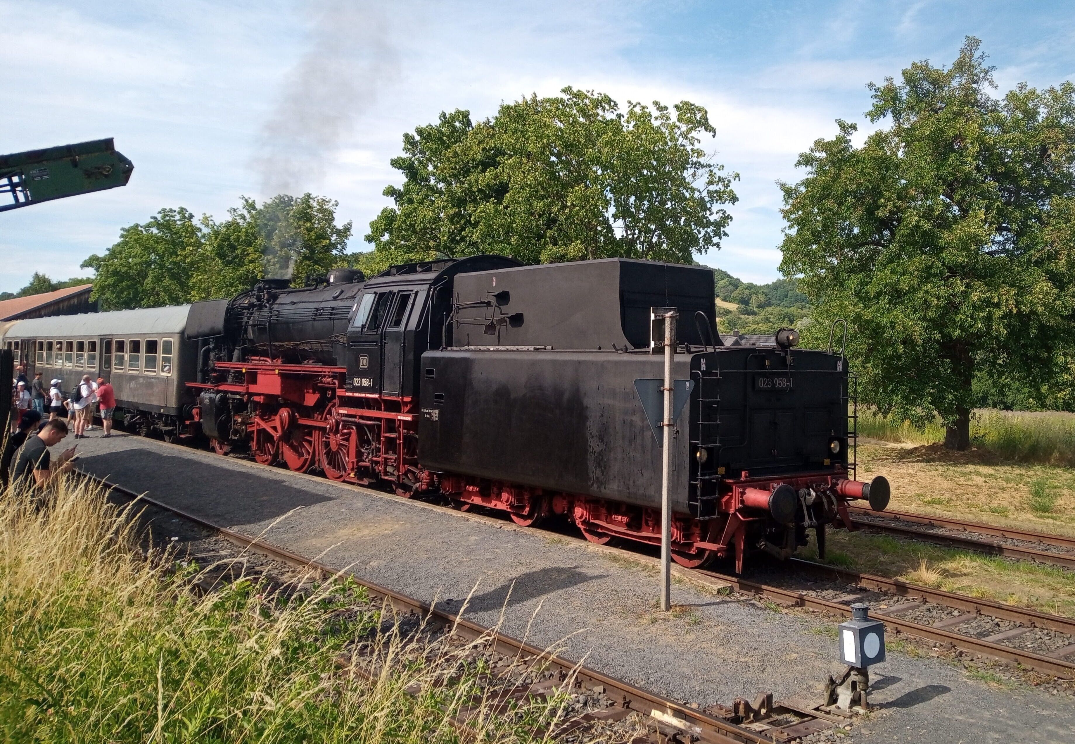 Eine Dampflokomotive auf Gleisen mit Bahnsteig und Bäumen im Hintergrund.