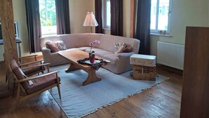 Un salon confortable avec un canapé, un fauteuil et une table basse. Il y a une horloge au mur et une fenêtre avec des rideaux.