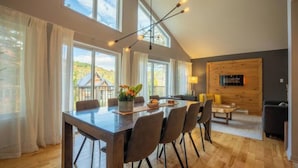 A spacious dining area with a long wooden table, multiple chairs, and a modern chandelier.