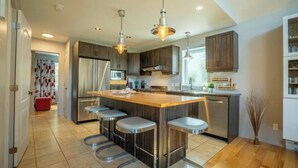 A modern kitchen with a central island, bar stools, stainless steel appliances, and pendant lighting.