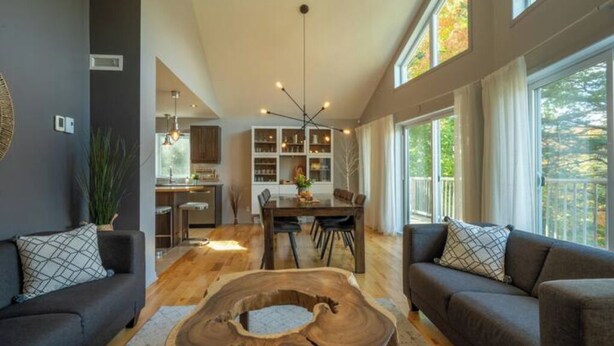 A modern living room with a wooden coffee table, dark sofas, and a dining area with a chandelier.