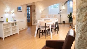 A cozy living room with a white sofa, a dining table with chairs, a white cabinet, and a large window providing natural light. - Charme rare sous les voûtes accommodation in Royat (Royat)