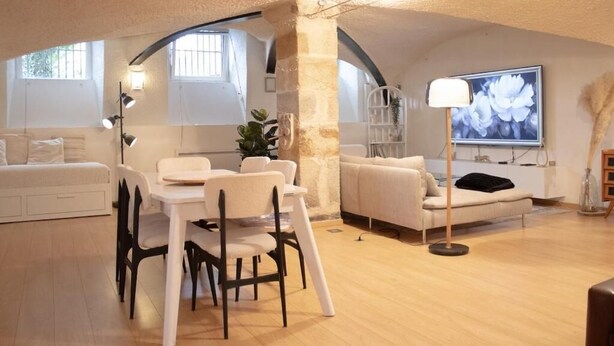 A spacious living area with a dining table, white sofas, and a large window with a flower painting. - Charme rare sous les voûtes accommodation in Royat (Royat)