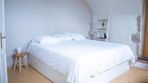 A bedroom with a white bed, a small wooden stool, and a white shelf with a plant. - Charme rare sous les voûtes accommodation in Royat (Royat)