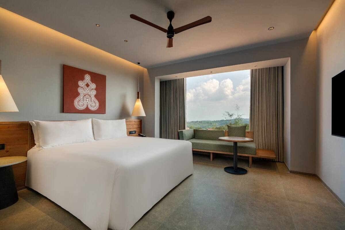 A hotel room with a large bed, a seating area with a table, a ceiling fan, and a view of the outdoors.