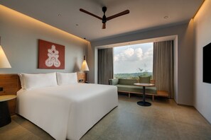 A hotel room with a large bed, a seating area with a table, a ceiling fan, and a view of the outdoors. - Greenpark Resort  and Spa Madikeri (Madikeri)