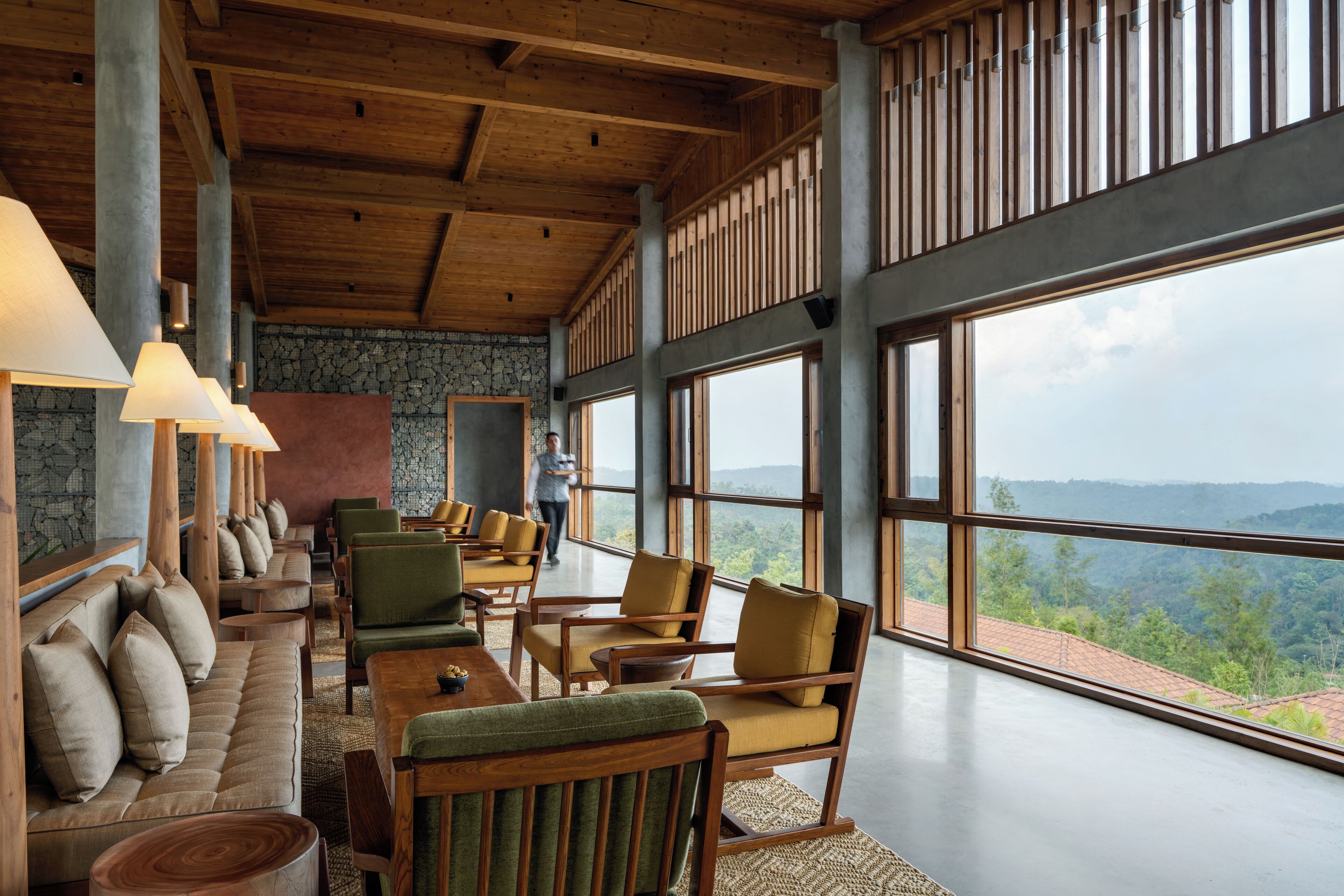 A spacious room with a high ceiling, large windows offering a view of the outdoors, and a seating area with sofas and chairs.