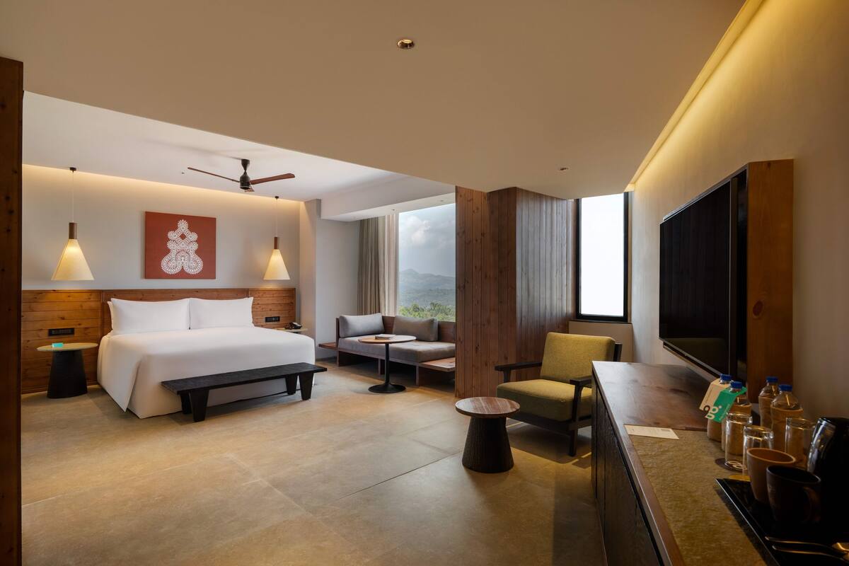 A modern hotel room with a large bed, a sofa, a desk, and a TV.