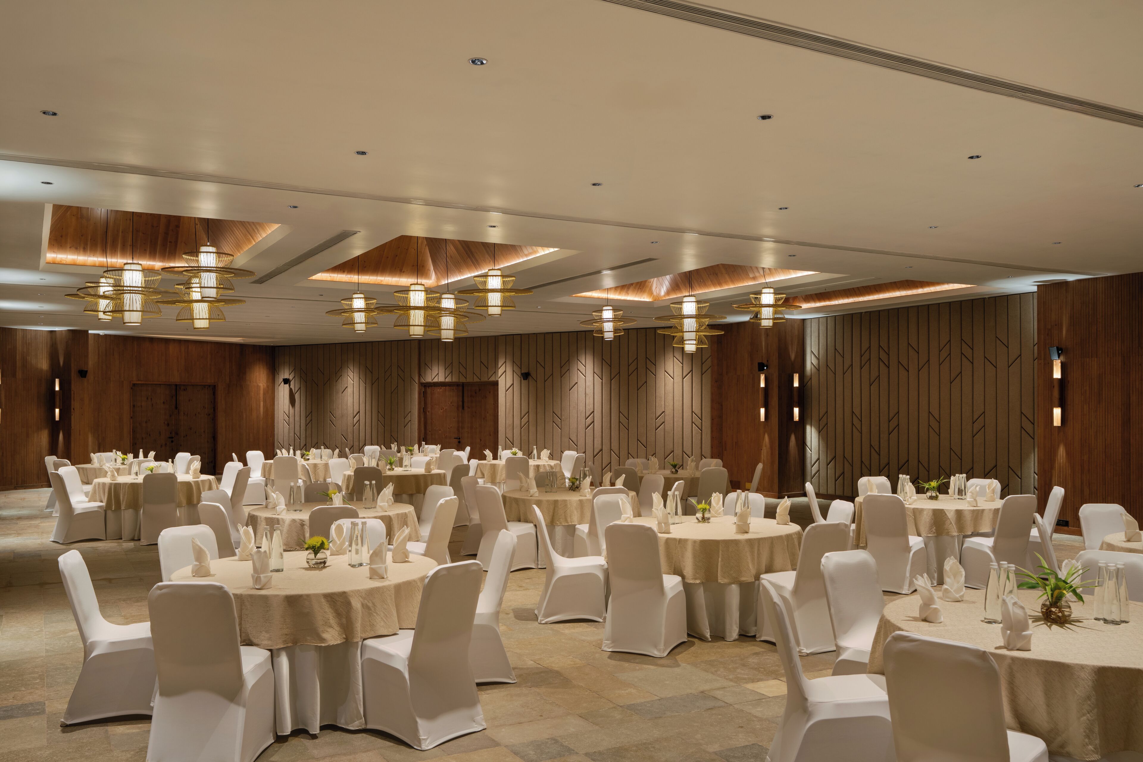 A banquet hall with round tables, white chairs, and chandeliers.
