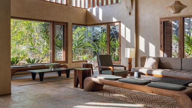 A spacious room with a high ceiling, large windows, and a cozy seating area with a sofa and chairs.