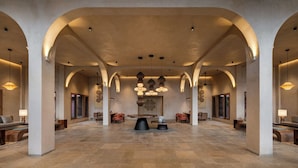 A spacious lobby with high ceilings, arched columns, and a central seating area with tables and chairs.