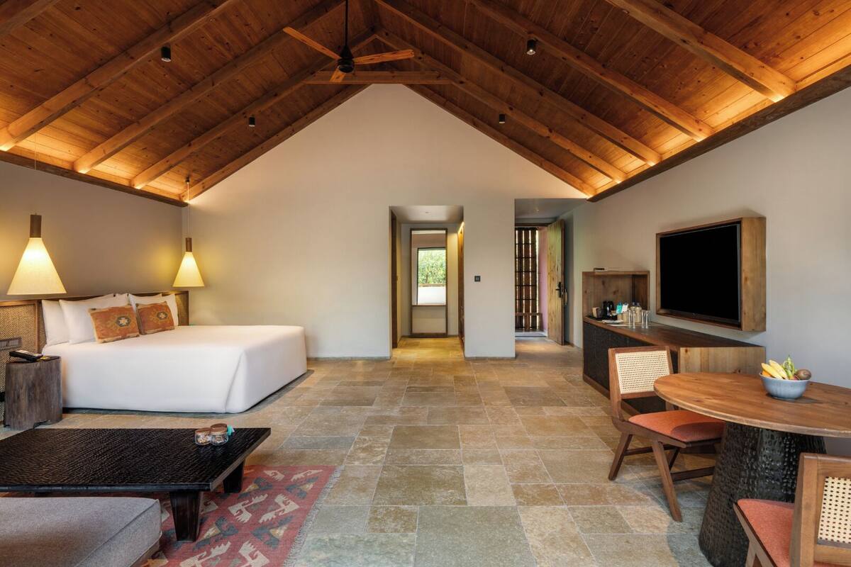 A spacious room with a high ceiling, a bed, a desk, a chair, and a television.