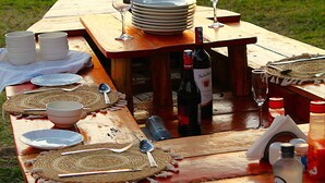 A wooden picnic table set up by a lake with plates, bowls, cutlery, and wine glasses. - Bayside Resort Lake Victoria (Mbita)