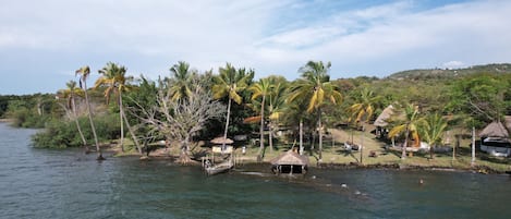A riverside view with palm trees, huts, and a boat.